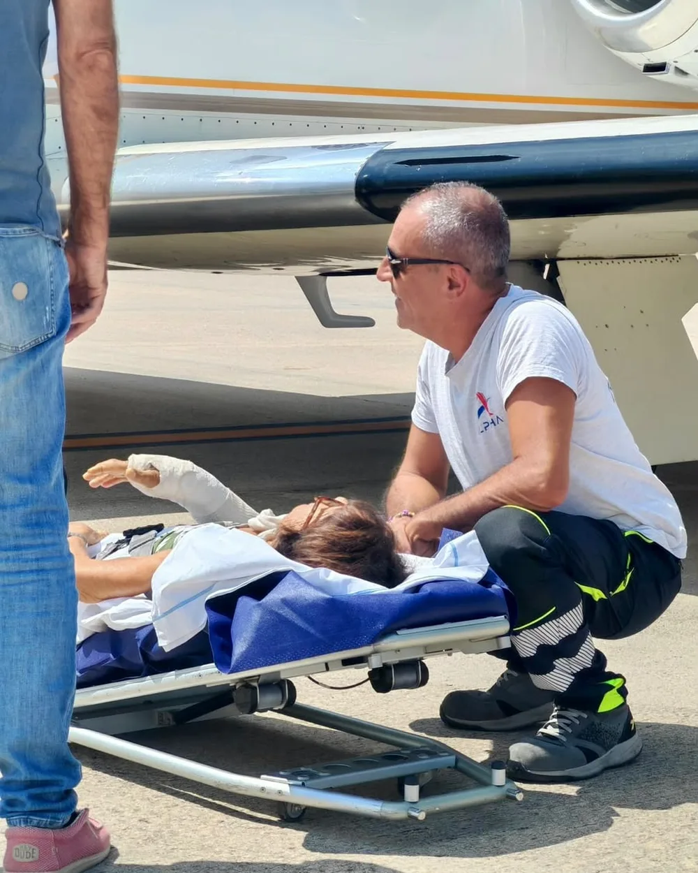 Un operatore ALPHA inginocchiato parla con un paziente disteso sulla barella