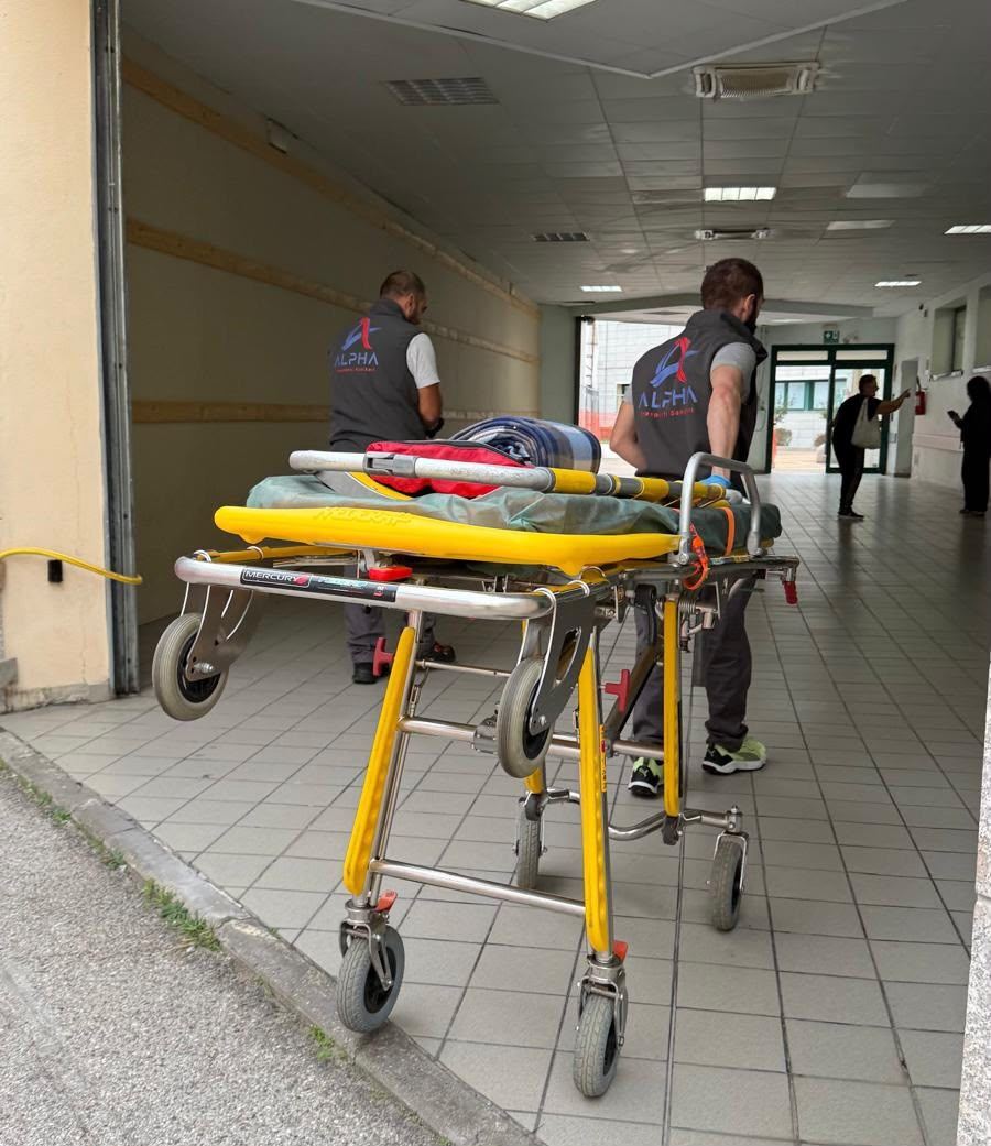Due operatori con la divisa ALPHA spingono la barella lungo il corridoio dell'ospedale