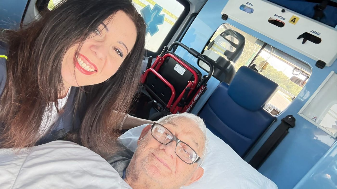 La nostra operatrice sorride accanto a un paziente sereno sulla barella, all'interno dell'ambulanza attrezzata con la sedia saliscale