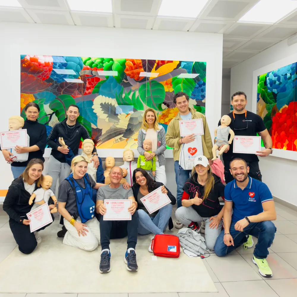 Un gruppo di corsisti in un'azienda mostra gli attestati di primo soccorso appena conseguiti insieme agli istruttori BasicLife, con i manichini in primo piano