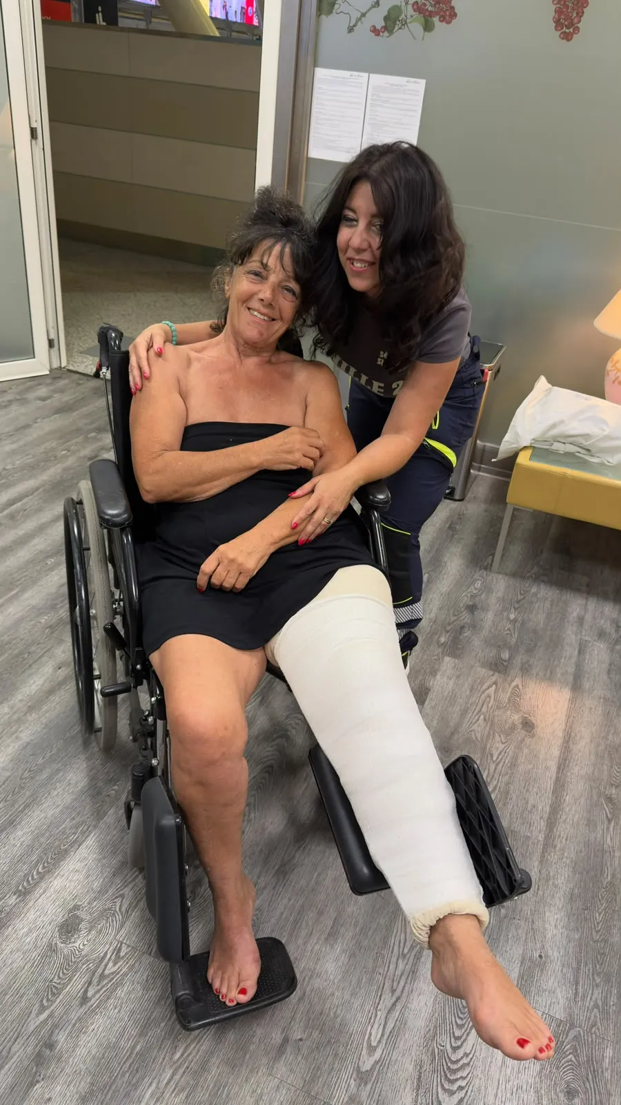 Miriam, operatrice ALPHA, sorride con una paziente con la gamba fasciata sulla sedia a rotelle, pronta per tornare a casa