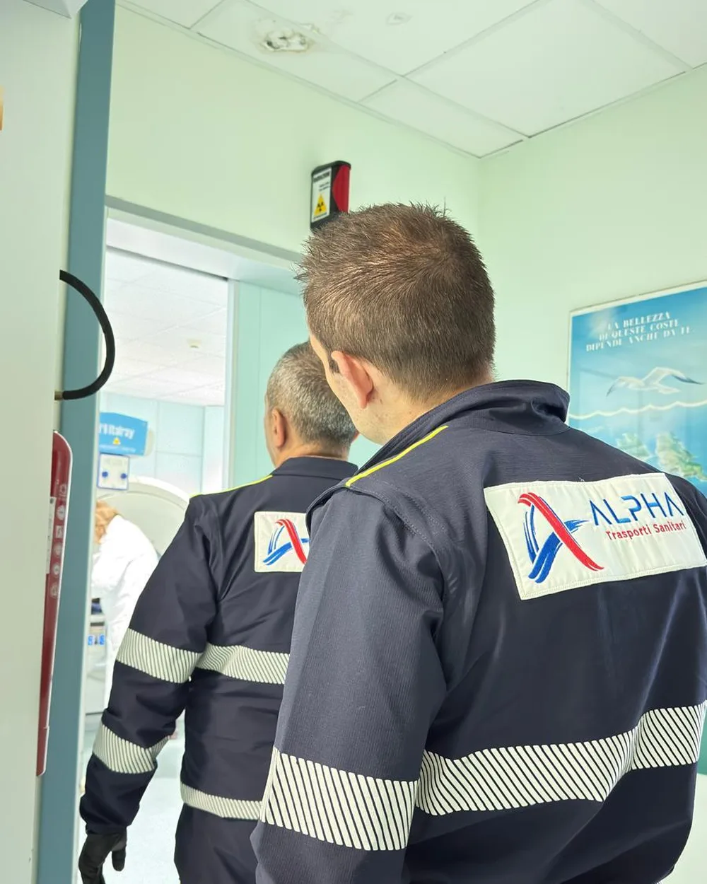 Un operatore ALPHA di spalle attende in un corridoio dell'ospedale davanti alle porte a vetri della diagnostica