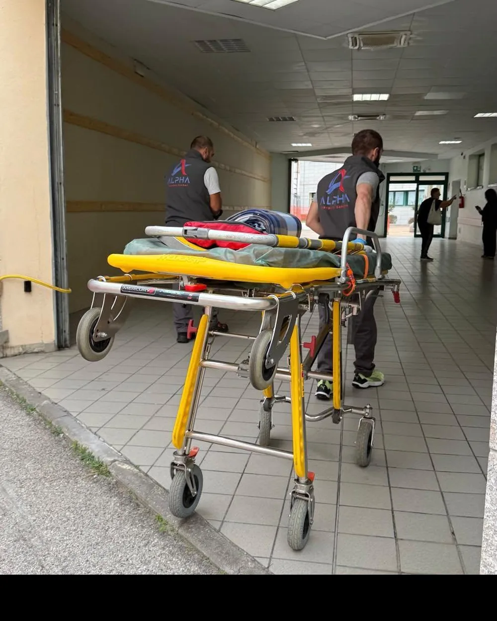 Due operatori ALPHA accompagnano la barella fino all'ingresso di una struttura riabilitativa