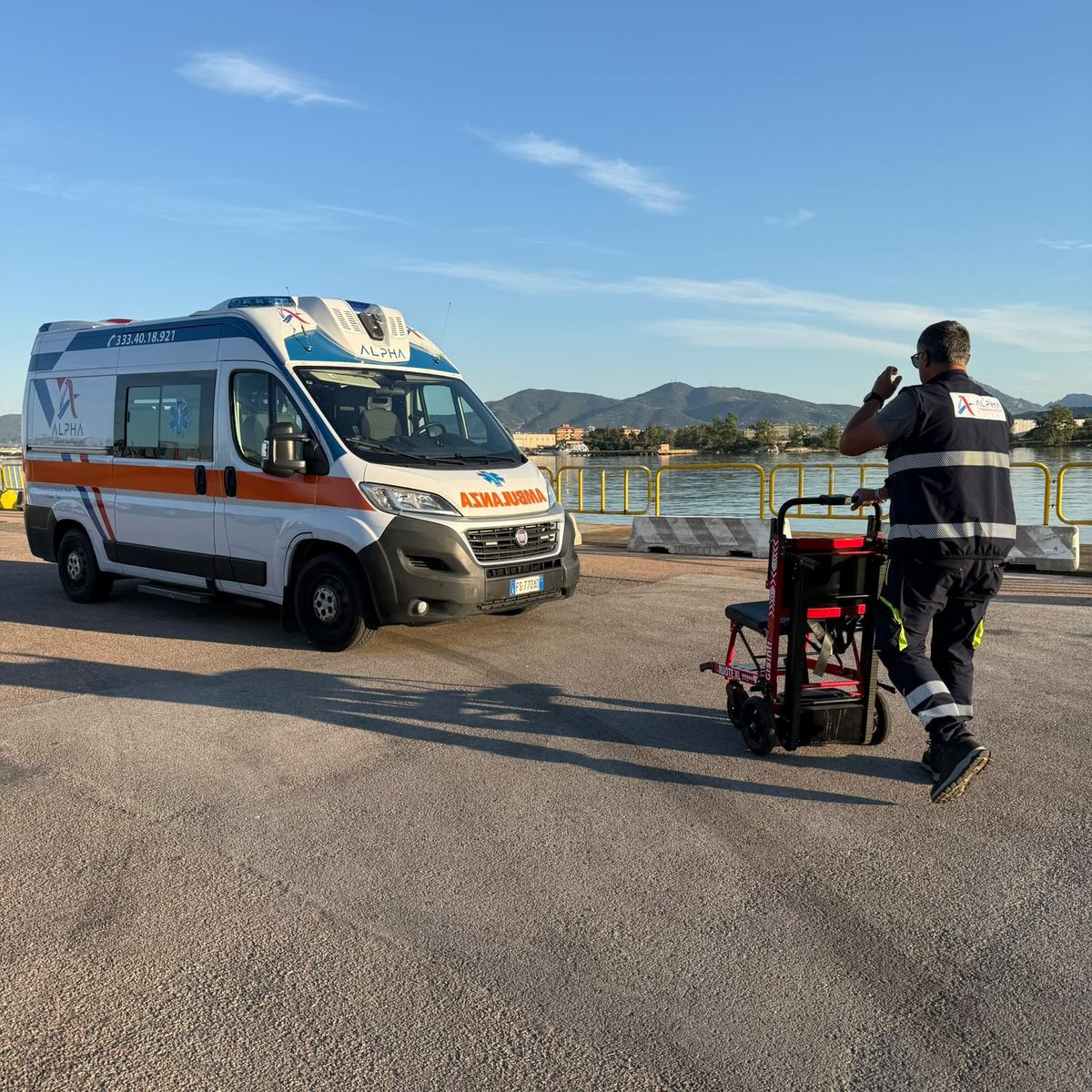 Un operatore ALPHA accompagna la sedia saliscale elettrica a cingoli con ruote XL verso l'ambulanza, in riva al mare