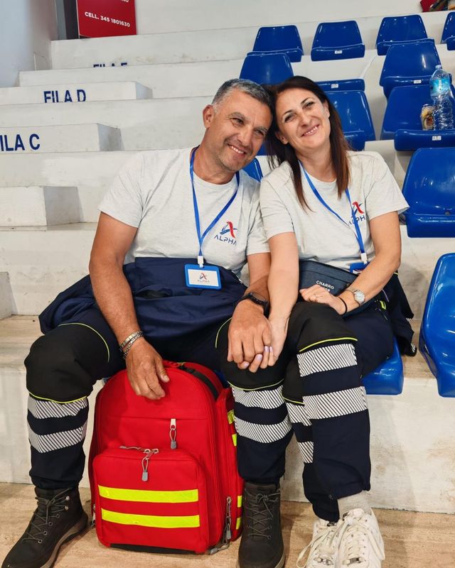 Gesuino e sua moglie Lina, entrambi volontari ALPHA, sorridono seduti accanto allo zaino di primo soccorso