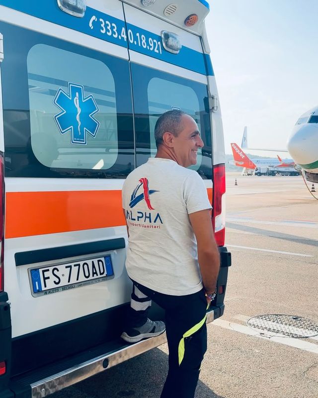 Sergio, il presidente di ALPHA, sorride accanto all'ambulanza in aeroporto